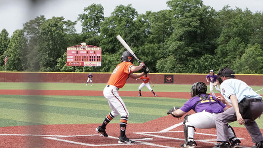 High school baseball player swinging the bat during a game on a sunny day, with teammates and spectators in the background.